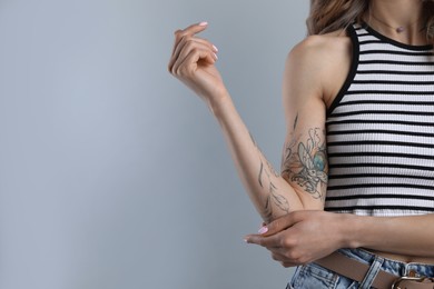 Photo of Beautiful woman with tattoos on arm against grey background, closeup. Space for text