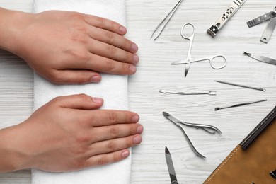 Man holding hands on towel near set of manicure tools at white wooden table, top view
