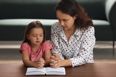 Mature woman with her little granddaughter praying together over Bible at home
