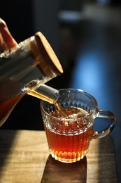 Pouring delicious tea into glass cup on wooden table, closeup