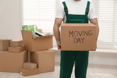 Man holding cardboard box with words MOVING DAY in room, closeup