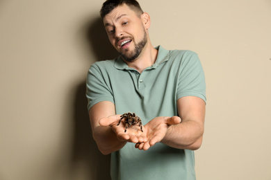 Scared man holding tarantula on beige background. Arachnophobia (fear of spiders)