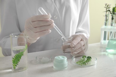Scientist making cosmetic product at white table in laboratory, closeup