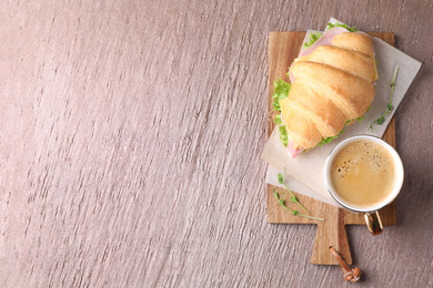 Tasty croissant sandwich with ham and cup of coffee on brown table, top view. Space for text