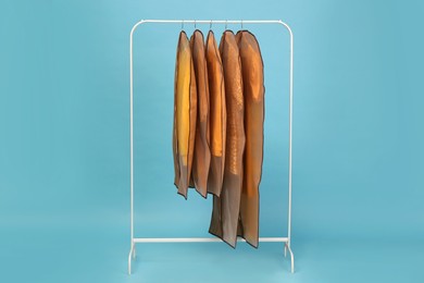 Garment bags with clothes on rack against light blue background