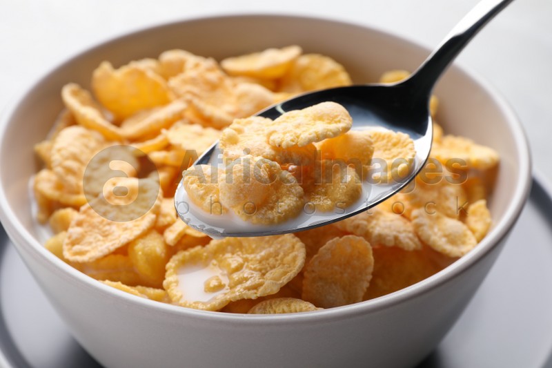 Spoon with tasty cornflakes and milk over bowl, closeup