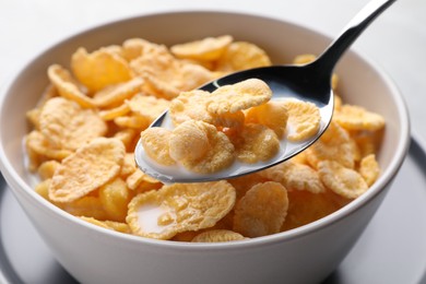 Spoon with tasty cornflakes and milk over bowl, closeup