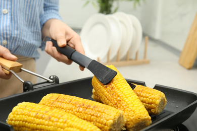 Woman taking corn from grill pan with tongs in kitchen, closeup