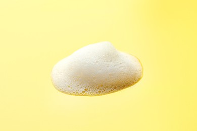 Photo of Drop of fluffy soap foam on yellow background