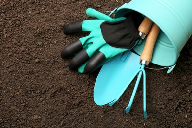 Photo of Overturned bucket with gardening tools and gloves on fresh soil, flat lay. Space for text