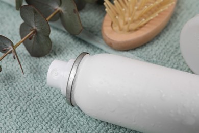 Dry shampoo spray, hairbrush and eucalyptus branch on towel, closeup