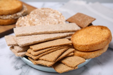 Plate of rye crispbreads, rice cakes and rusks on white marble table