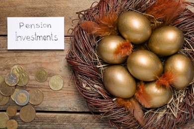 Many golden eggs, coins and card with phrase Pension Investments on wooden table, flat lay