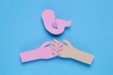 Photo of Woman's health. Newborn paper figure and hands on light blue background, flat lay
