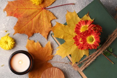 Photo of Book decorated with chrysanthemum flowers, autumn leaves and scented candle on light gray textured table, flat lay