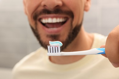 Man holding brush with toothpaste against blurred background, closeup