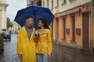 Lovely young couple with umbrella walking under rain on city street