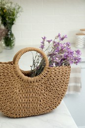 Stylish beach bag with beautiful bouquet of wildflowers on white table in kitchen