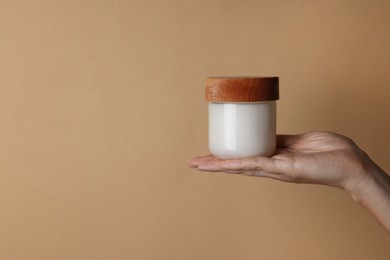 Photo of Woman holding jar of cosmetic product on beige background, closeup. Space for text