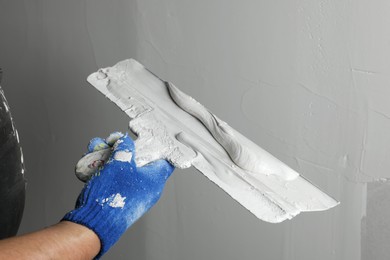 Professional worker holding putty knife with plaster indoors, closeup