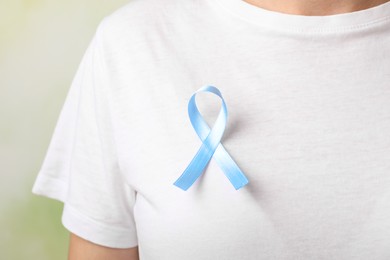 Photo of Woman with light blue awareness ribbon against blurred green background, closeup