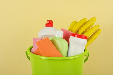 Bucket with different cleaning supplies against beige background, closeup