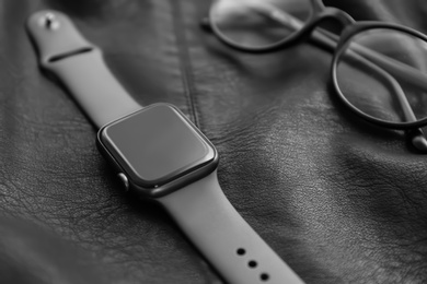 Stylish smart watch and glasses on black leather fabric, closeup