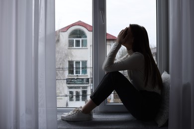 Unhappy young woman crying near window indoors, space for text. Loneliness concept
