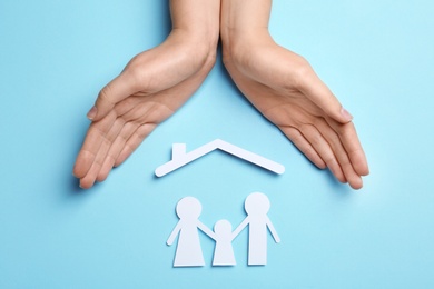 Woman holding hands over paper silhouettes of family and house roof on color background, top view. Life insurance concept