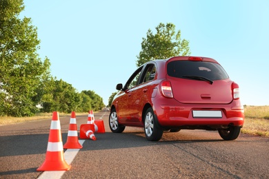 Red car near fallen traffic cones outdoors. Failed driving school exam