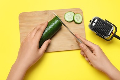 Woman making ASMR sounds with microphone and cucumber on yellow background, top view