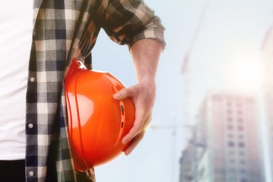 Man with orange hard hat at construction site with unfinished building, closeup. Space for text 