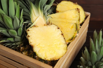Photo of Tasty cut pineapples in wooden crate on table, closeup
