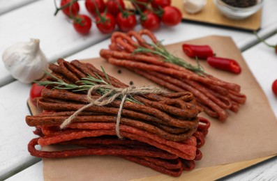 Photo of Delicious kabanosy with rosemary, peppercorn, chilli and tomatoes on white wooden table, closeup