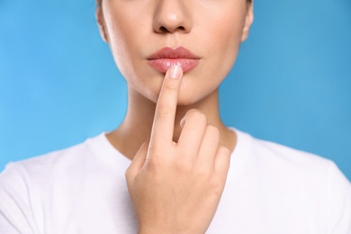 Woman with herpes touching lips on light blue background, closeup