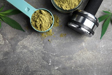 Hemp protein powder, fresh leaves and dumbbell on grey table, flat lay. Space for text