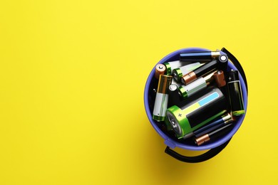 Image of Used batteries in bucket on yellow background, top view. Space for text