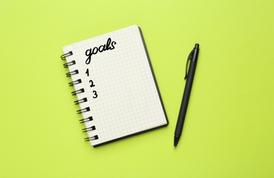 Notebook with goal list and pen on green background, flat lay
