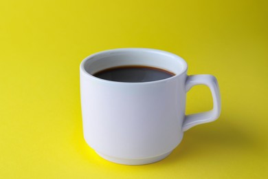 White mug of freshly brewed hot coffee on yellow background