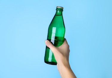 Woman holding glass bottle with water on light blue background, closeup