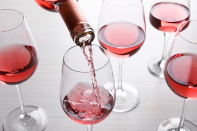 Pouring rose wine from bottle into glasses on wooden table, closeup