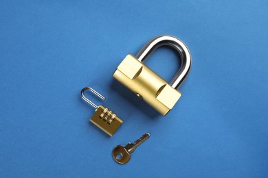 Modern padlocks with key on blue background, flat lay