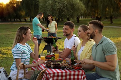 Happy friends with drinks and food at barbecue party in park