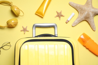 Flat lay composition with suitcase and sun protection products on yellow background