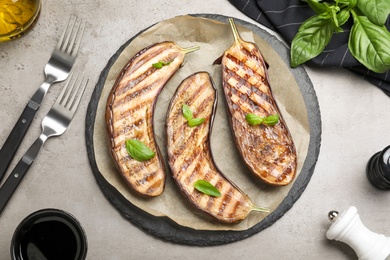 Delicious grilled eggplant halves with basil served on grey table, flat lay