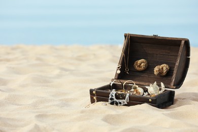 Photo of Open wooden chest with treasures on sandy beach, space for text