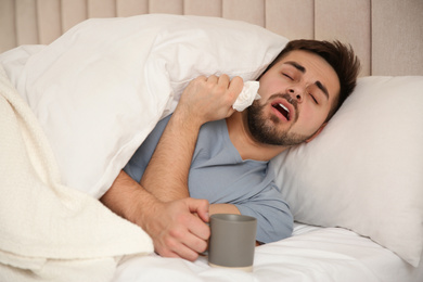 Sick young man with cup of hot drink in bed at home. Influenza virus