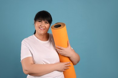 Happy overweight mature woman with yoga mat on light blue background. Space for text