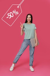 Happy woman pointing at tag with discount on pink background. Special promotion