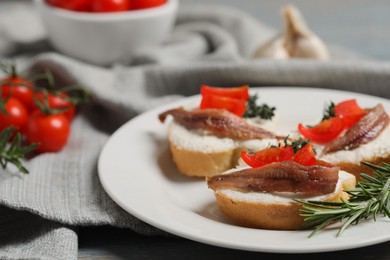 Photo of Delicious sandwiches with cream cheese, anchovies and tomatoes on grey wooden table, closeup. Space for text